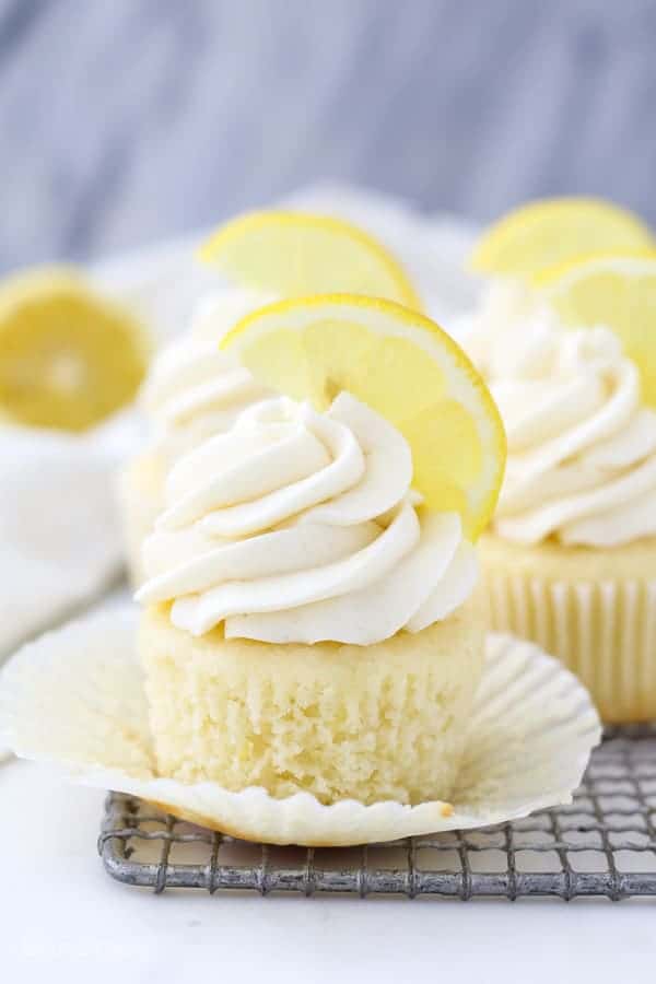 An unwrapped cupcake sitting on a wire rack with a big swirl of lemon frosting and a lemon garnish on top