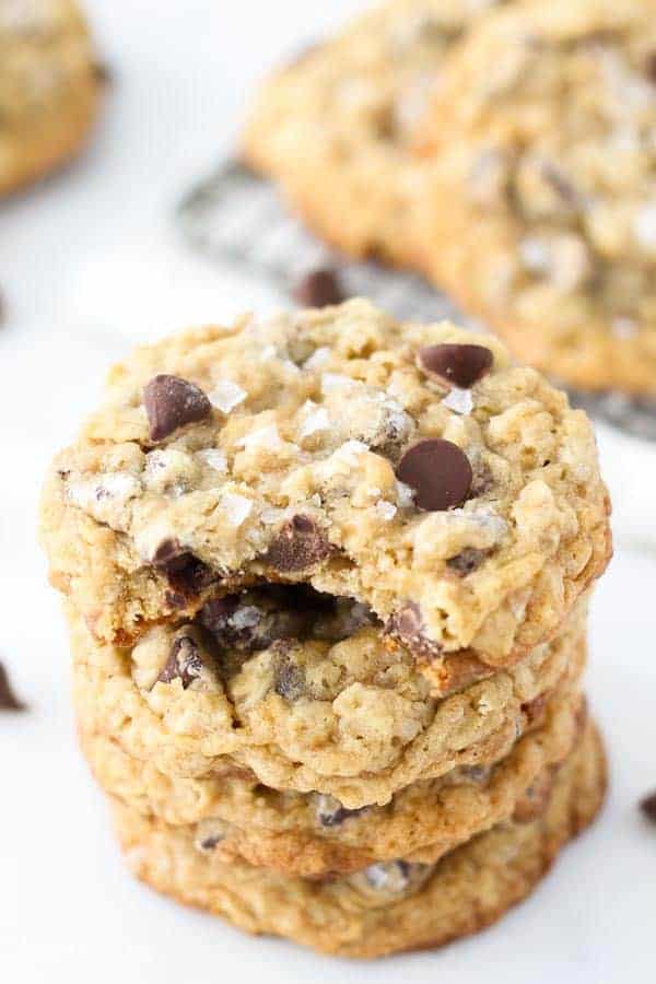 A big stack of chocolate chip oatmeal cookies, the cookie on top has a big bite taken out of it