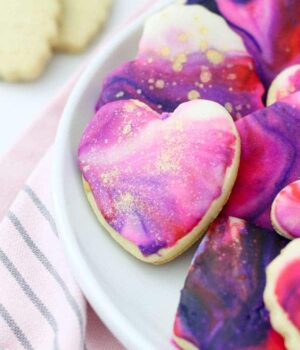 A beautiful mini heart shaped sugar cookie with marble icing and gold pearl dust decorated in Valentine's day colors