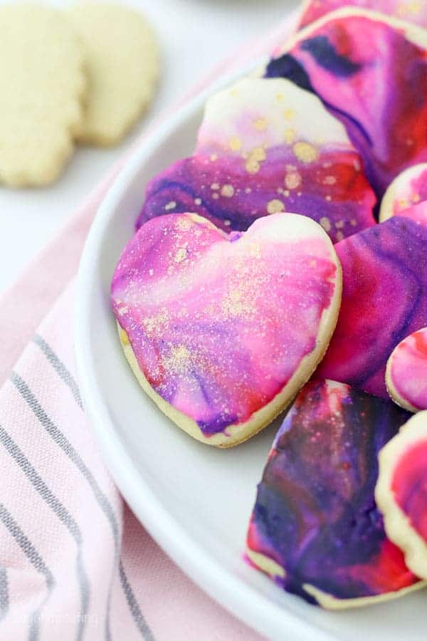 A beautiful mini heart shaped sugar cookie with marble icing and gold pearl dust decorated in Valentine's day colors