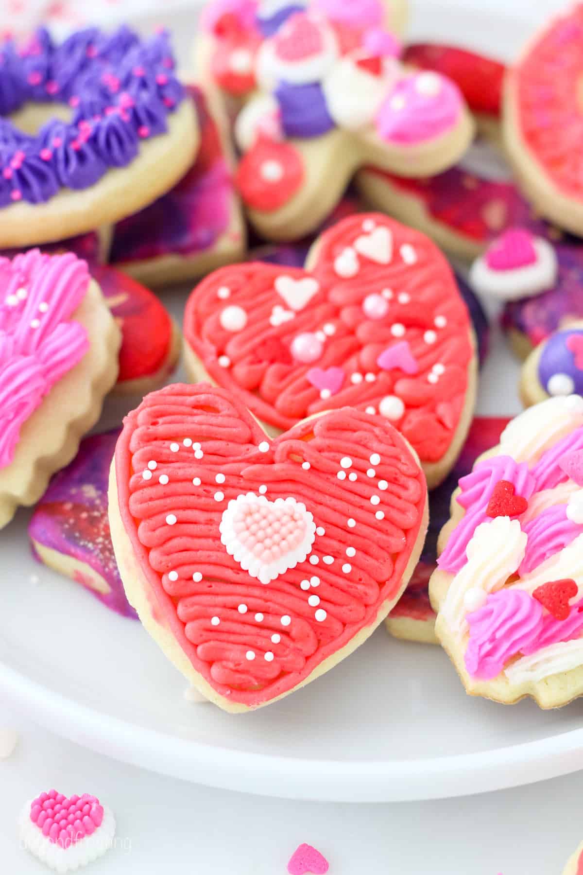 Close up of assorted Valentine's Day sugar cookies decorated with icing and frosting on a white plate.