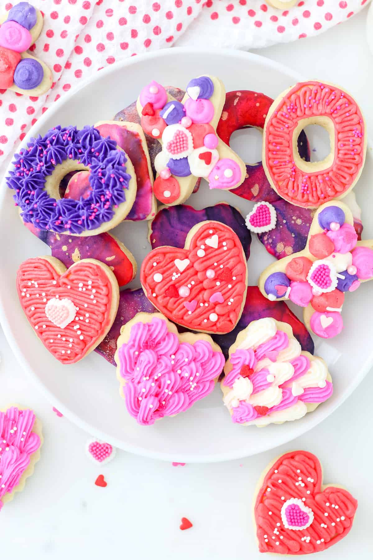 Overhead view of assorted Valentine's Day sugar cookies decorated with icing and frosting on a white plate.