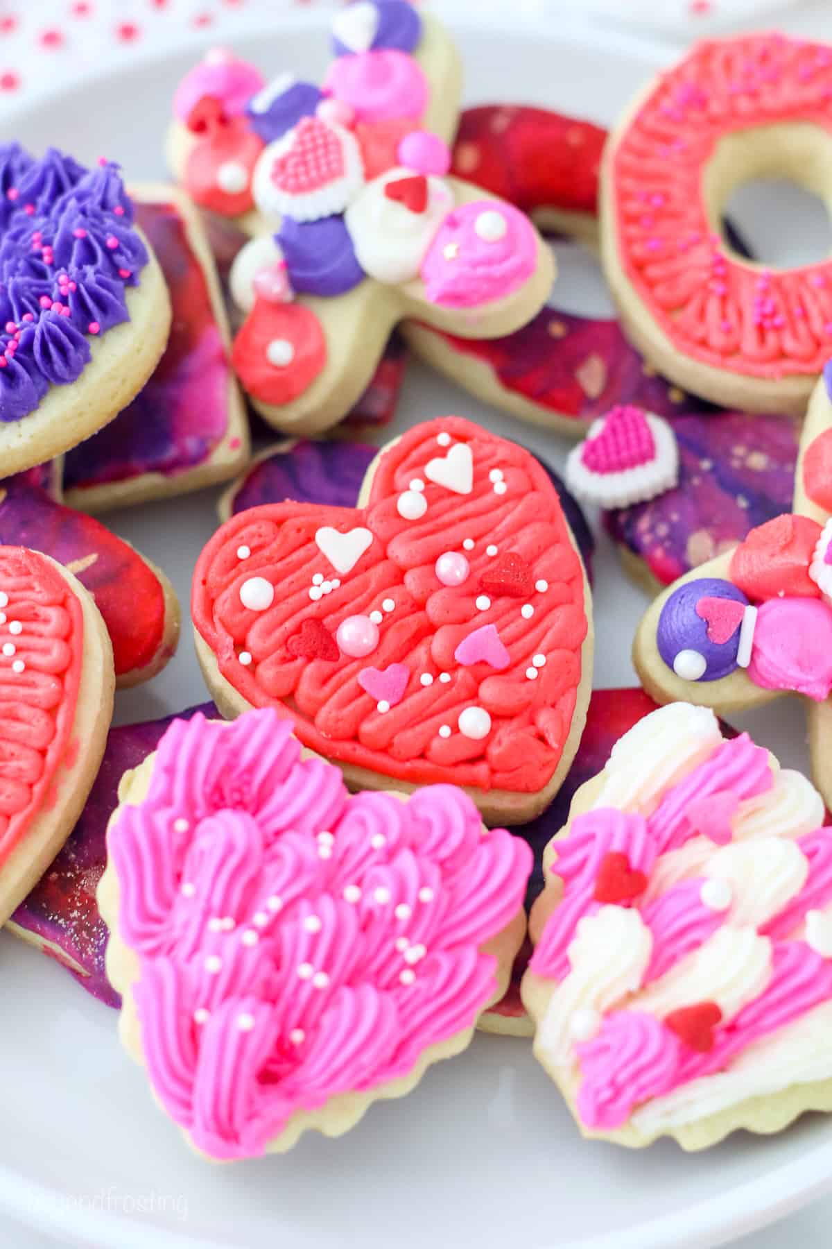 Close up of assorted cut-out Valentine's Day sugar cookies decorated with icing and frosting on a white plate.