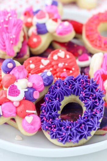 Assorted cut-out Valentine's Day sugar cookies decorated with icing and frosting on a white plate.