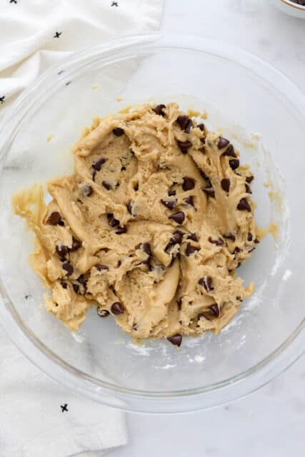 Overhead view of chocolate chip cookie dough in a glass mixing bowl.
