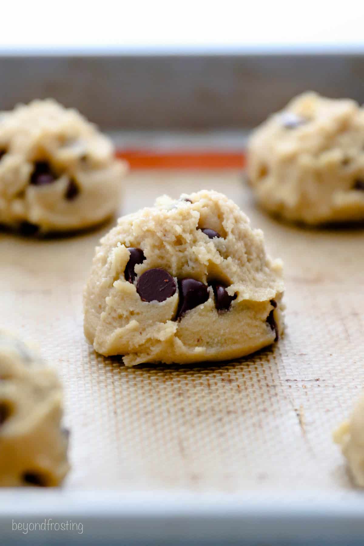 Close up of chocolate chip cookie dough balls on a lined baking sheet.
