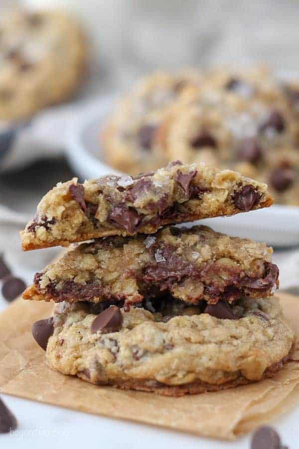 A stack of chewy oatmeal chocolate chip cookies, one cookie is broken in half, showing the ooey gooey centers and melted chocolate chips
