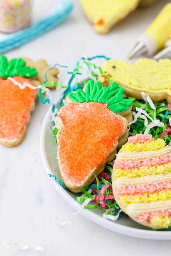 Sugar cookie shaped like a carrot decorated with buttercream, orange sprinkles and green frosting.