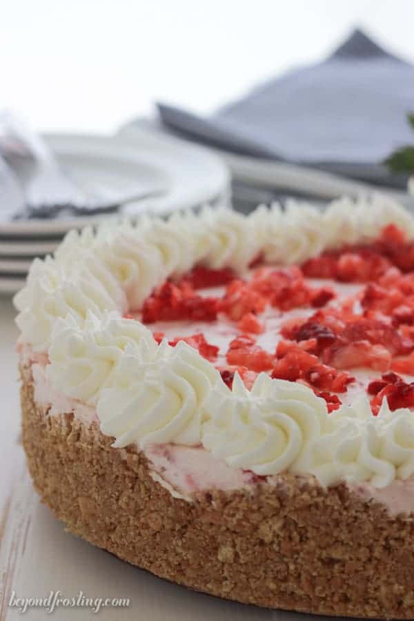 A whole stawberry pie with a graham cracker crust and whipped cream swirls. It's back light with some plate, napkins and silver wear in the background.