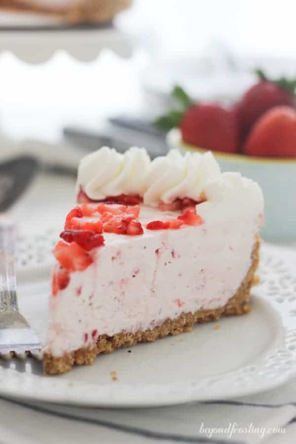 A gorgeous slice of strawberry pie on a white ruffled edge plate with a silver fork in the background.