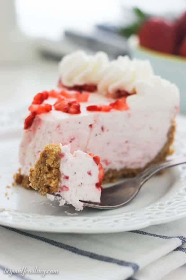 A silver fork with a bite of strawberry pie on it, and a slice of pie blurred out in the background.