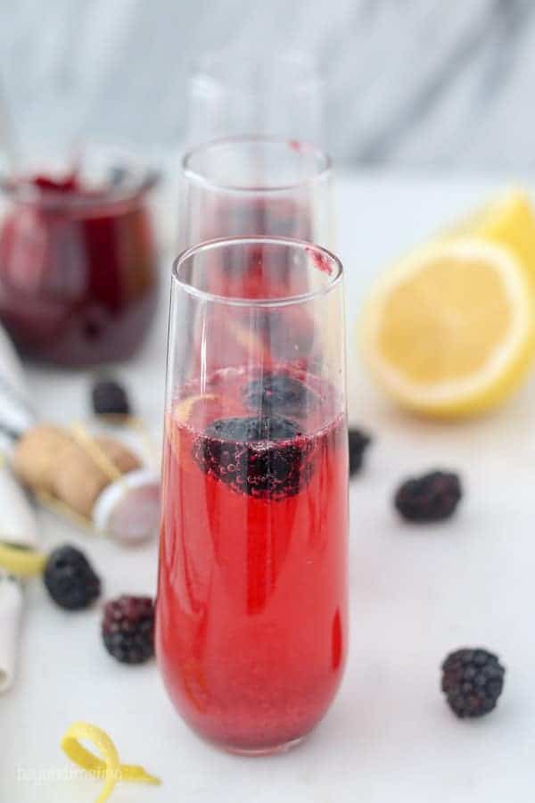 Three French 75 cocktails garnished with blackberries and a lemon twist