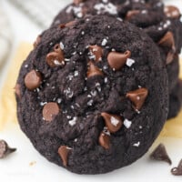 Close up of a double chocolate chip cookie leaning against a stack of cookies.