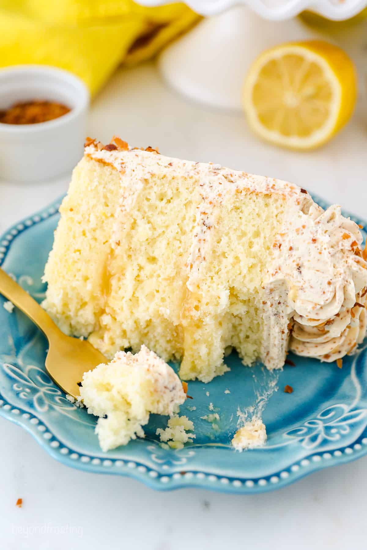 A partially eaten slice of lemon coconut cake on a blue plate, next to a fork.