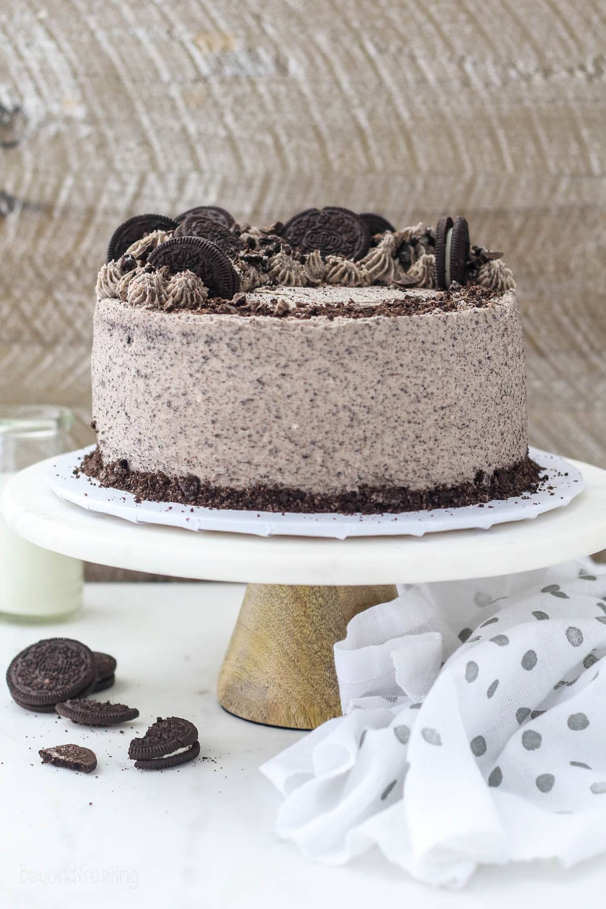 A whole frosted Oreo chocolate cake garnished with Oreo cookies on a cake stand.