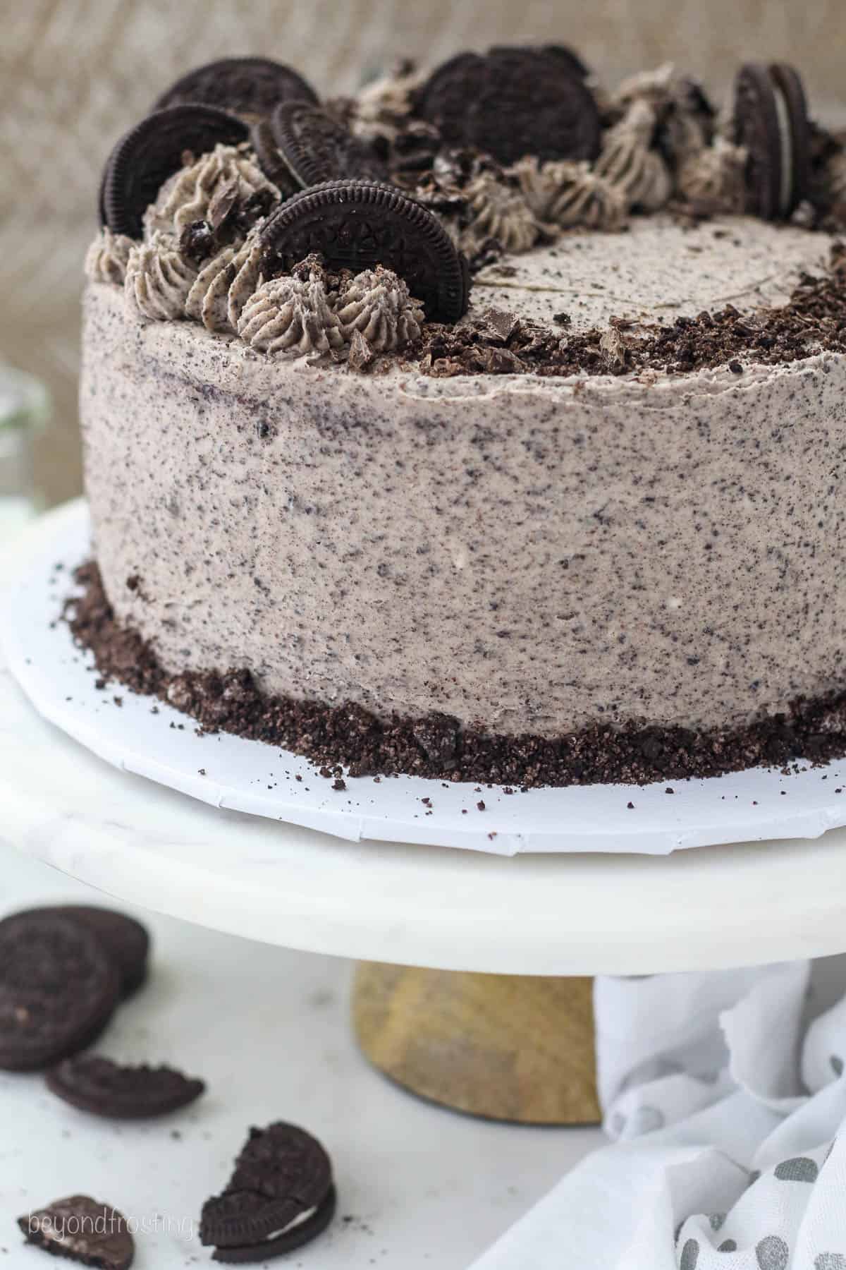 Close up of a whole frosted Oreo chocolate cake garnished with Oreo cookies on a cake stand.