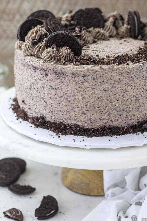 A whole Oreo cake sitting on a marble cake stand, the cake is topped with crushed Oreos