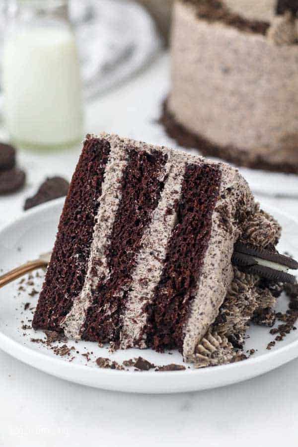 A 3 layer chocolate cake with Oreo icing on a large white cake plate sprinkled with chocolate shavings