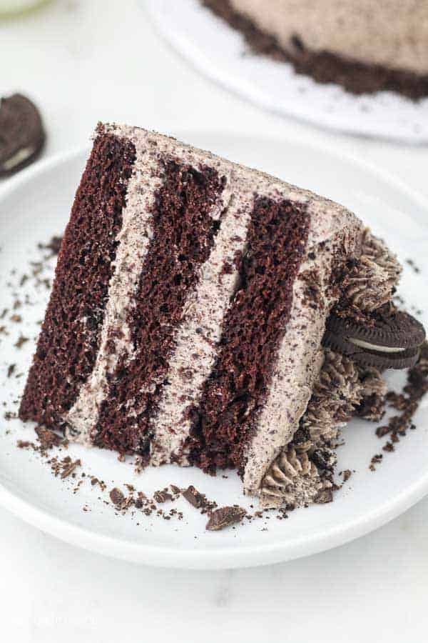 Un pastel de chocolate de 3 capas con glaseado Oreo en un plato grande de pastel blanco espolvoreado con virutas de chocolate