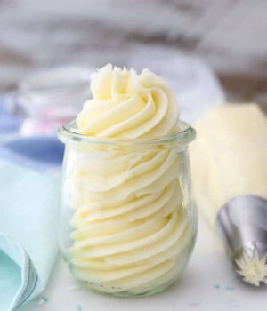 A small jar of piped vanilla buttercream with a full piping bag sitting next to it