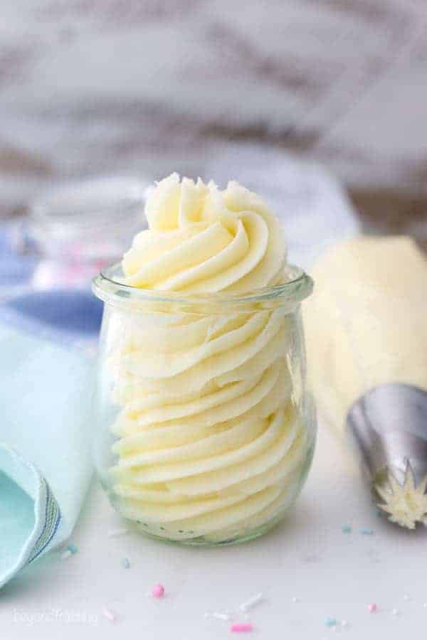 A small jar of piped vanilla buttercream with a full piping bag sitting next to it