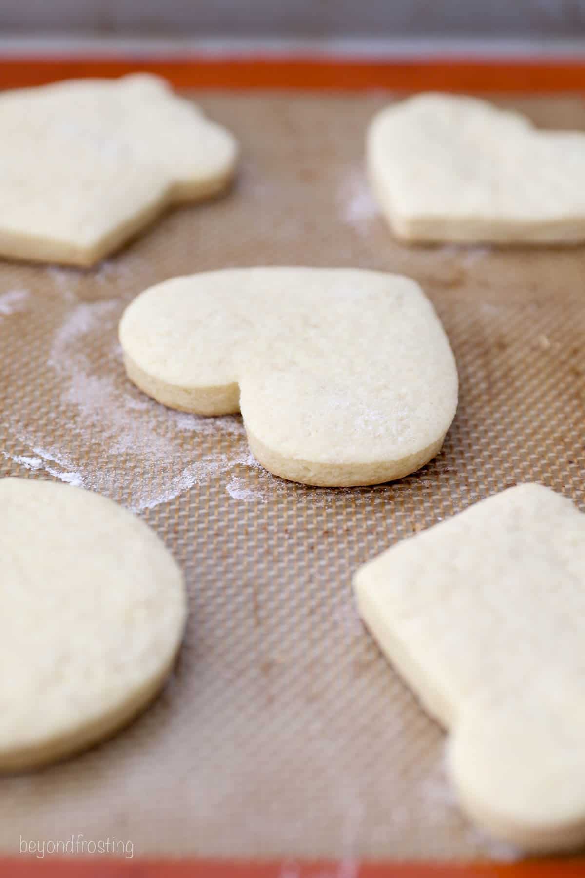 Close up view of a baked, heart-shaped sugar cookies on a Silpat lined baking sheet.