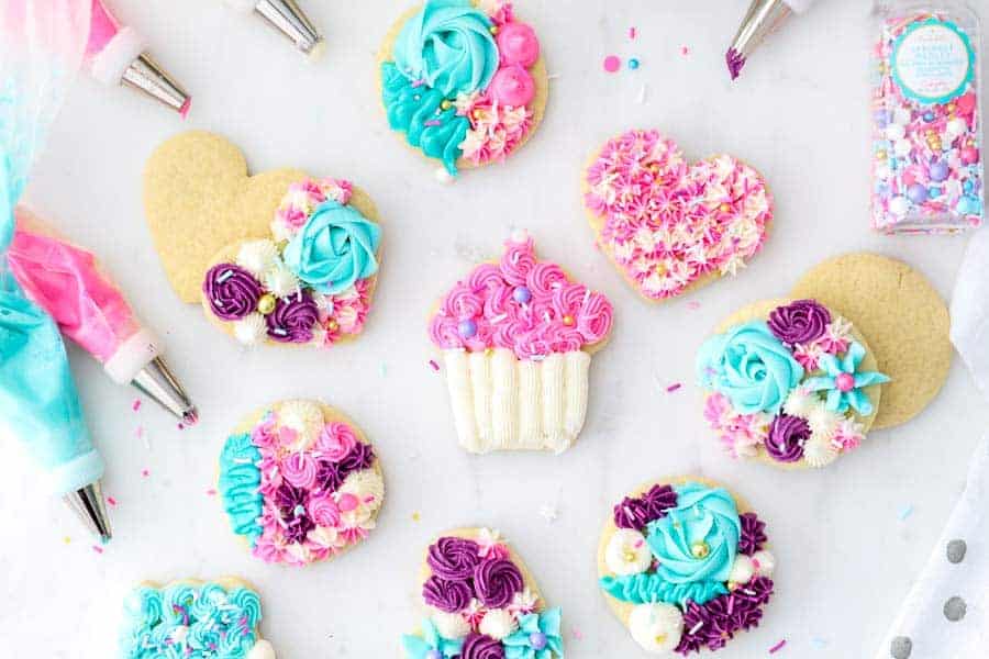 An overhead shot of the most gorgeous sugar cookies decorated with pink, purple, teal and white buttercream and Sweetapolita Sprinkles.