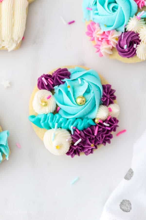A gorgeous sugar cookie decorated with purple, teal and white buttercream with roses, and flowers.
