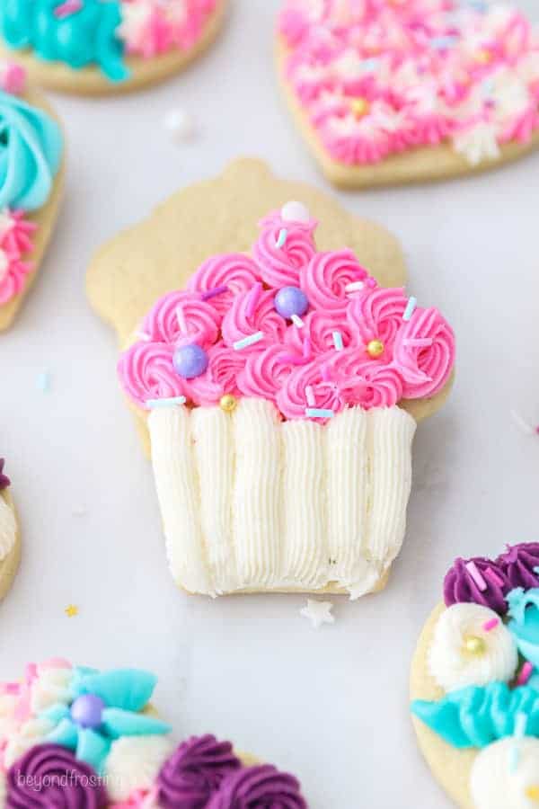 A cupcake shaped sugar cookie decorated with pink and white buttercream and sprinkles.