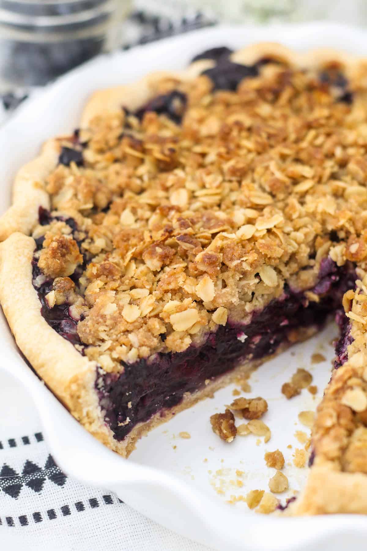 Blueberry crumble pie in a round pie dish with a slice missing.