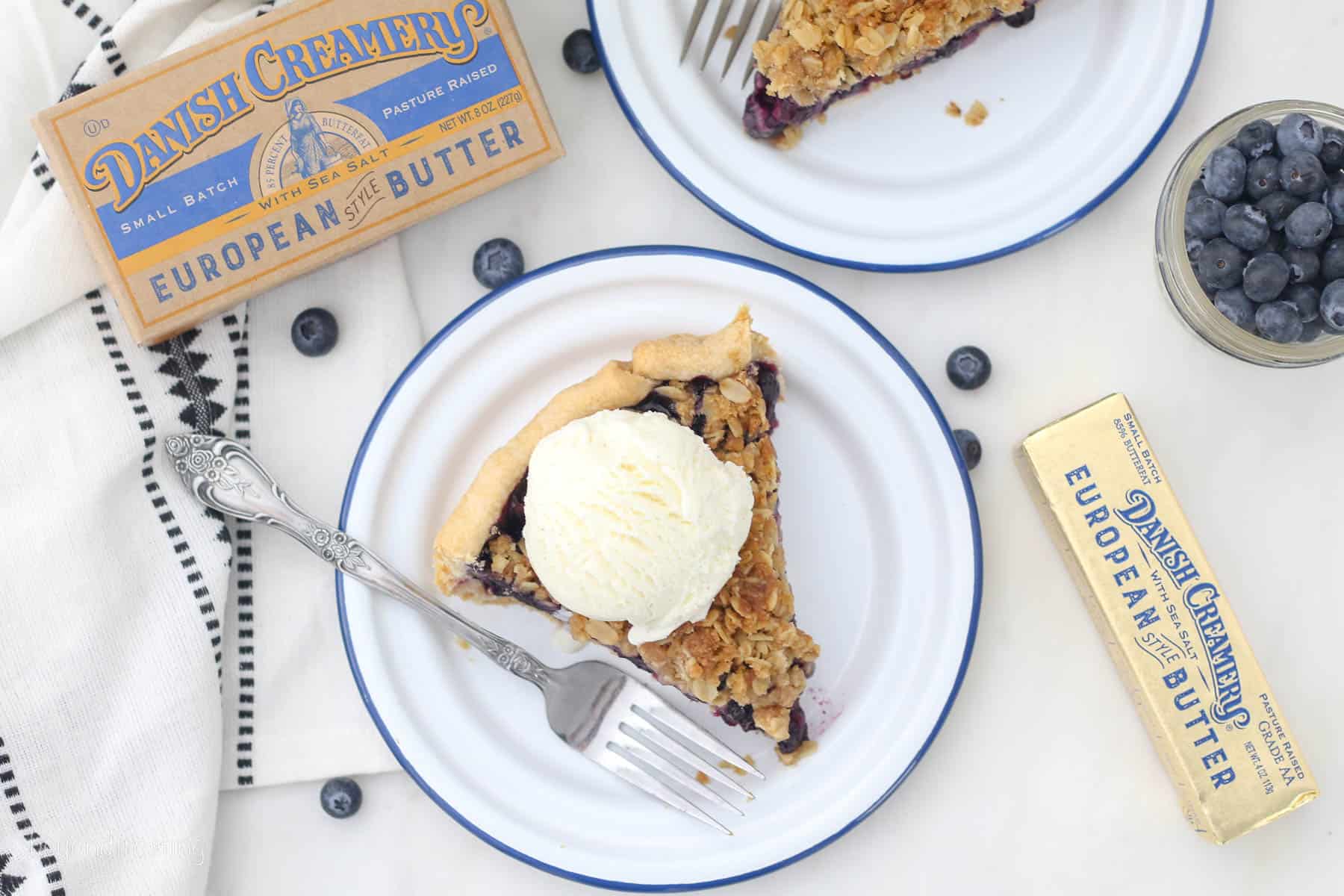 Overhead view of a slice of blueberry crumble pie on a plate, topped with a scoop of vanilla ice cream.
