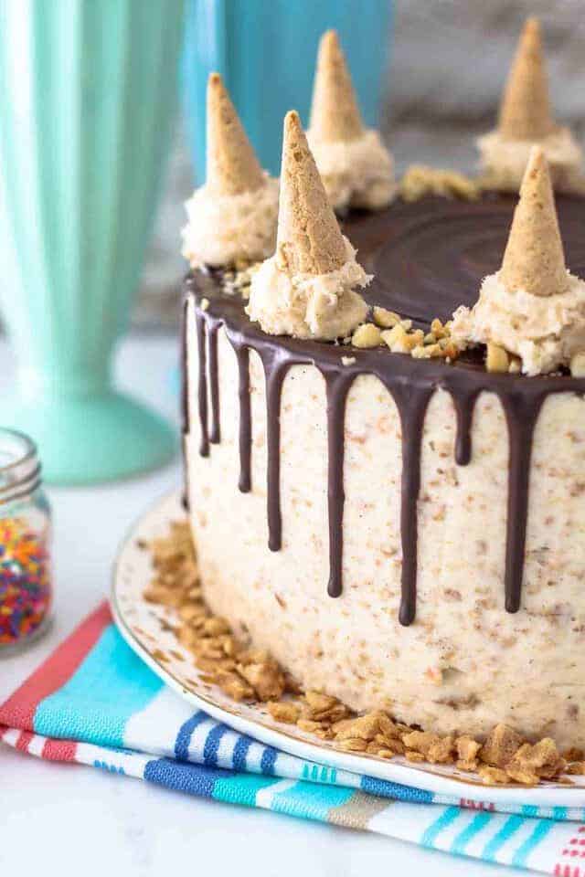 A close up shot of a Drumstick layer cake, with drippy chocolate ganache and mini cones on top