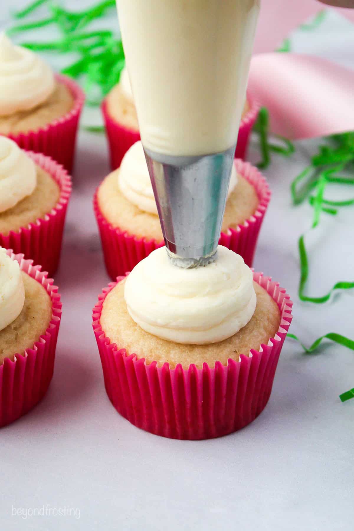 Make adorable Easter bunny cupcakes with chocolate ears following this easy step-by-step tutorial. They’re the perfect Easter cupcakes! A piping bag piping frosting on top of a cupcake.