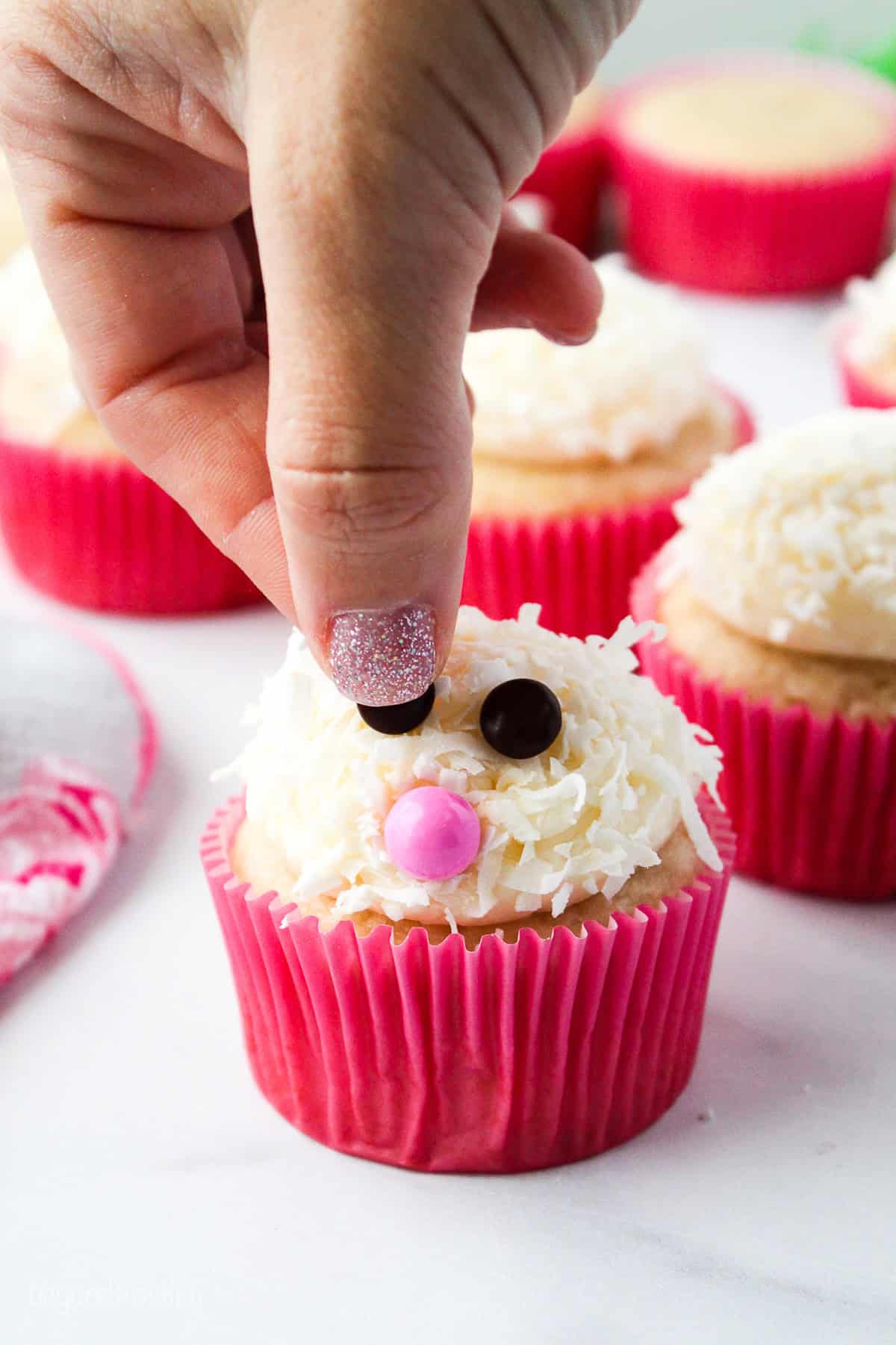 Make adorable Easter bunny cupcakes with chocolate ears following this easy step-by-step tutorial. They’re the perfect Easter cupcakes! A hand placing a chocolate chip "eye" onto a frosted bunny cupcake.
