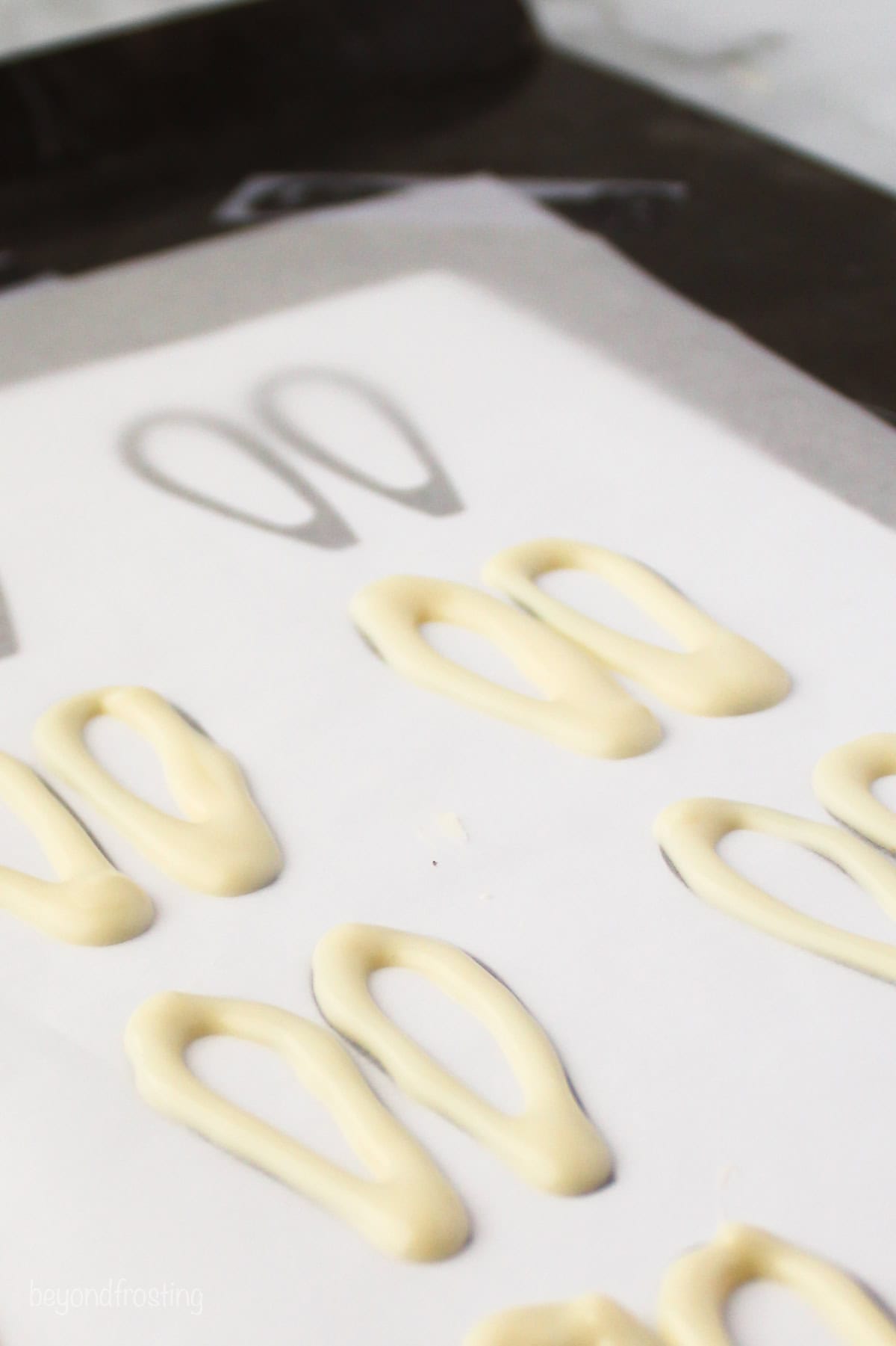 Make adorable Easter bunny cupcakes with chocolate ears following this easy step-by-step tutorial. They’re the perfect Easter cupcakes! White chocolate draw in the shape of bunny ears on a sheet of parchment paper.