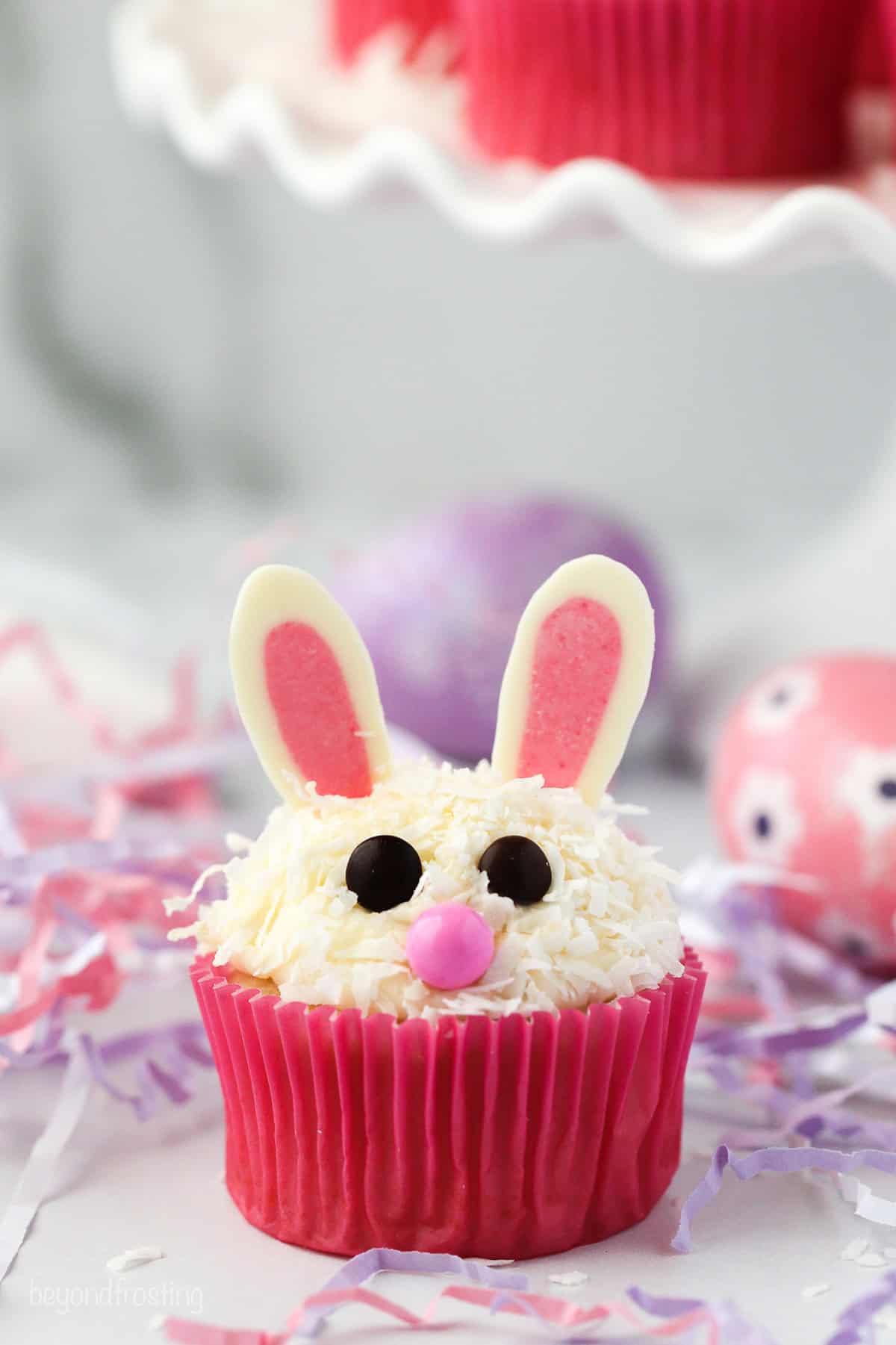 Make adorable Easter bunny cupcakes with chocolate ears following this easy step-by-step tutorial. They’re the perfect Easter cupcakes! An Easter bunny cupcake in a pink liner on a countertop.
