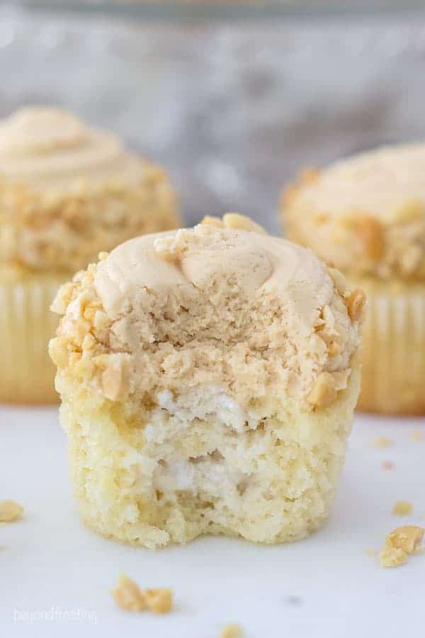 A cupcake with a big bit missing is showing the inside of the cupcake, filled with marshmallow creme and topped with frosting. It also have crushed peanuts on top