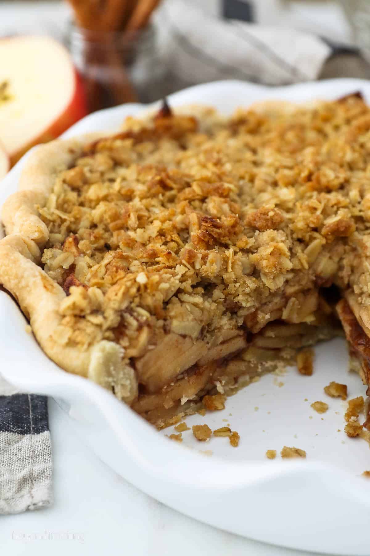 Apple crumble pie in a pie plate with a slice missing, showing layers of apples inside.