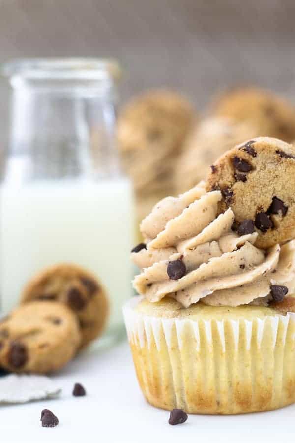 A close up shot of a cupcake with a big swirl of frosting, mini chocolate chips and topped with a mini chocolate chip cookie