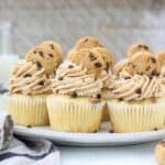 This horizontal image features several chocolate chip cookie cupcakes on a gray plate. The cupcakes are topped with a big swirl of frosting a mini chocolate chip cookies on top.