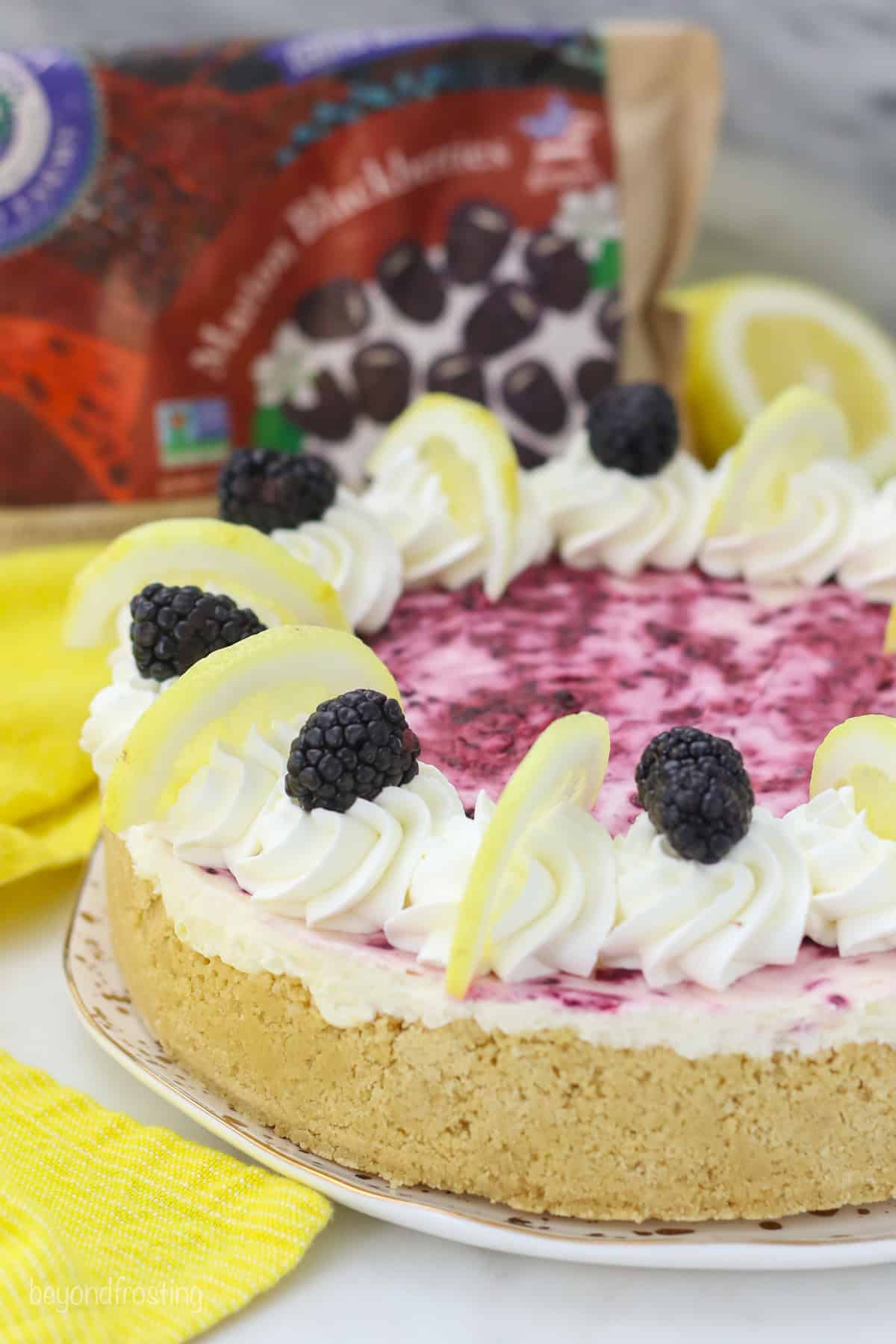 A no-bake blackberry lemon cheesecake decorated with swirls of whipped cream and garnished with lemon wedges and fresh blackberries.