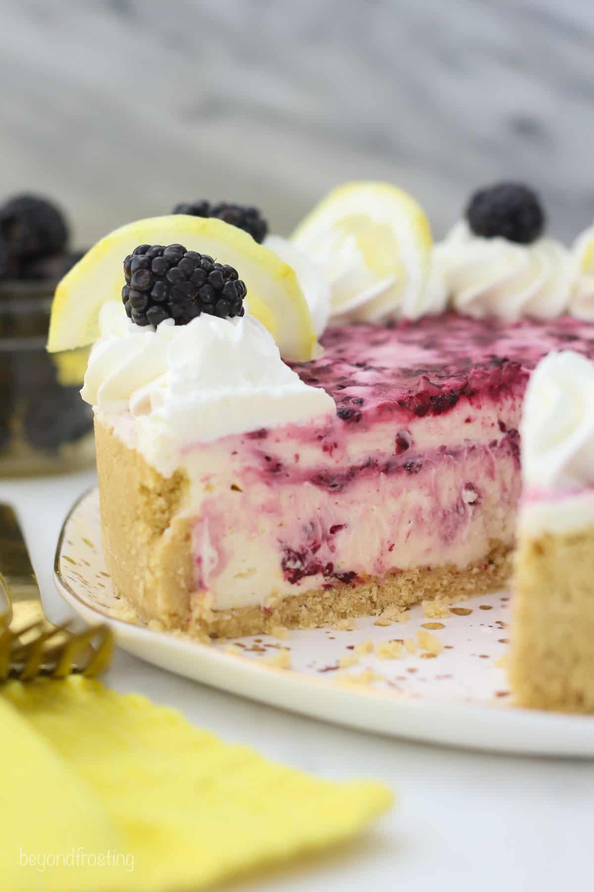 A no bake blackberry lemon cheesecake garnished with whipped cream and fresh blackberries with a slice missing.