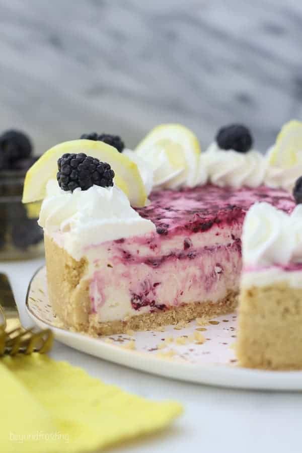 A whole no-bake lemon cheesecake with a slice missing showing the inside of the cheesecake which has swirls of blackberry sauce