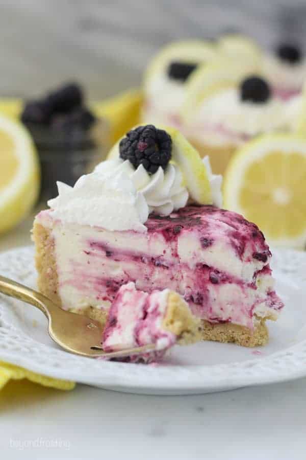 A no-bake lemon cheesecake with swirls of blackberries, it's got a bite taken out of it, and a gold fork sitting on a white plate