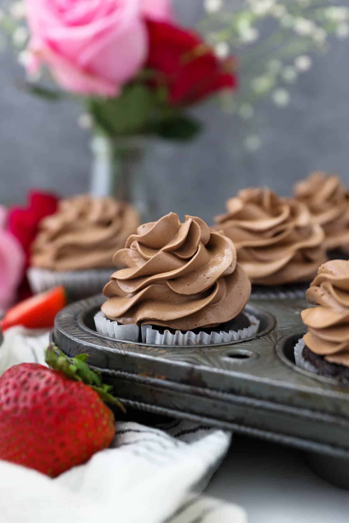 Cupcakes frosted with chocolate Swiss meringue buttercream in a muffin tin.