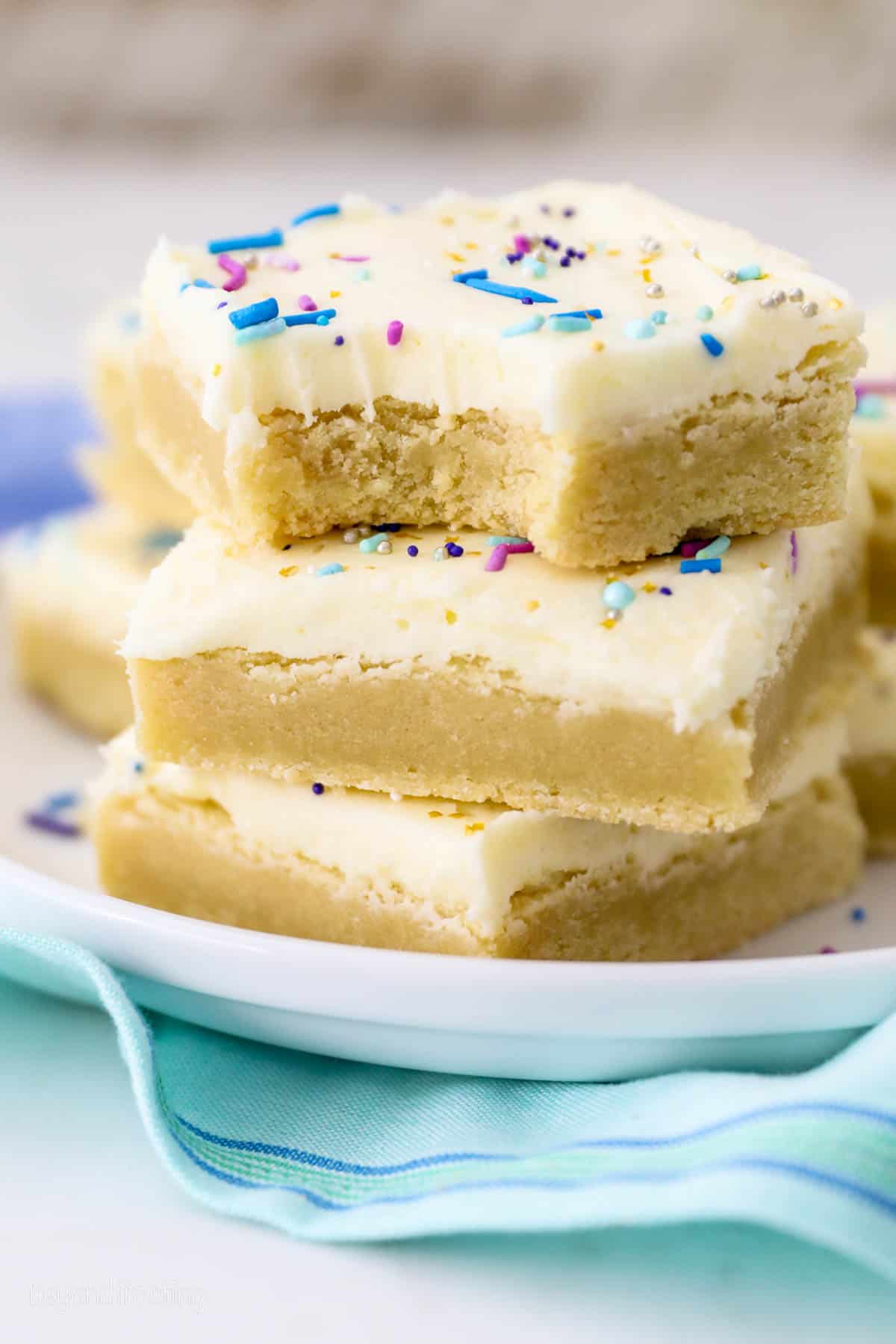 Three frosted sugar cookie bars stacked on top of one another, with a bite missing from the top cookie bar.