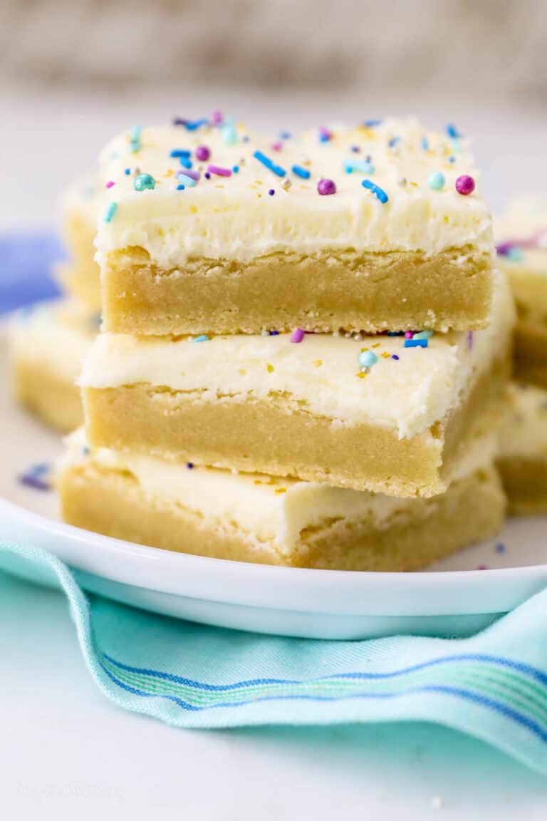 Three frosted sugar cookie bars stacked on top of one another on a plate.