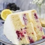 A close up shot of a lemon cake showing all the beautiful blackberries on the inside and the layers of lemon curd. The cake is sitting on a blue and white plate.