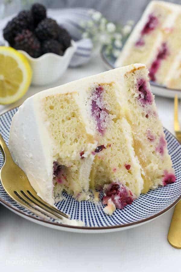 A giant slice of lemon cake layered with blackberries and lemon curd. There's a few bites missing showing the inside of the cake.