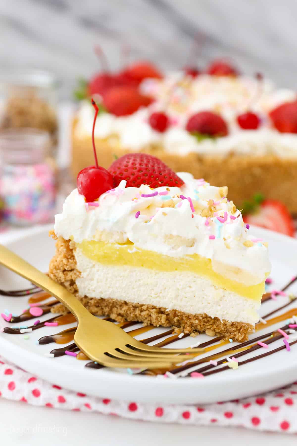 Banana split pie has all the flavors you love in a banana split, with creamy no-bake cheesecake, banana pudding, and all the sundae toppings! A slice of banana split pie topped with whipped cream, maraschino cherries, and sprinkles on a plate with the rest of the no-bake pie in the background.